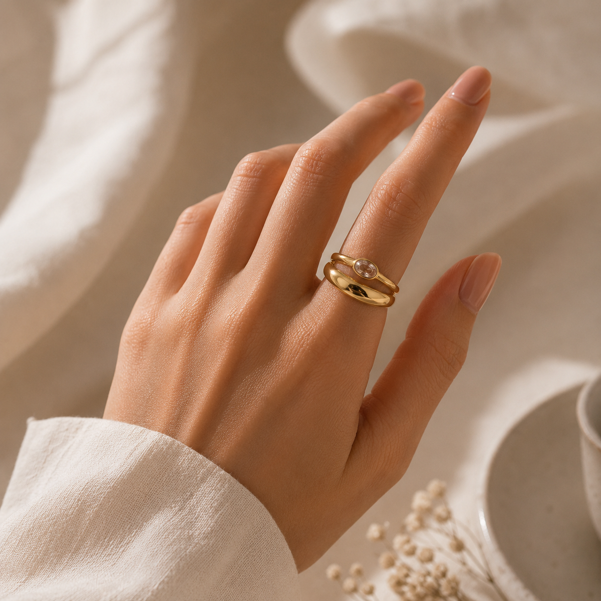 Hand wearing a gold ring with a pearl on a soft beige background